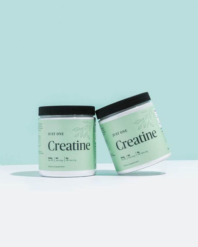 Two jars of Just One Creatine on a white tabletop against a mint wall